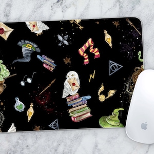 May include: A black mouse pad with a whimsical Harry Potter themed design. The design features a white owl, a stack of books, a green potion, a golden snitch, and a red and gold scarf. The background is a dark blue with stars and glitter.