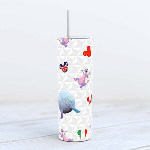 Könnte beinhalten: Ein weißer Becher mit Strohhalm, der mit einem Muster aus lila und weißen Figuren, roten Mickey-Maus-Köpfen und einer blau-weiß gemusterten Kugel verziert ist. Der Hintergrund ist ein weißes geometrisches Muster.