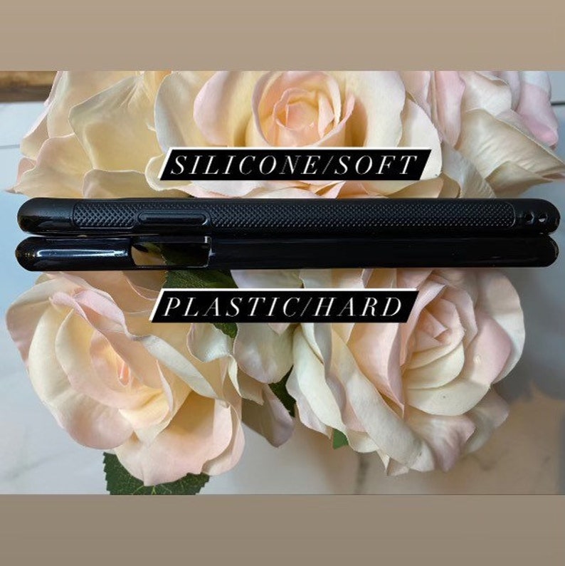 Op de afbeelding: Twee zwarte telefoonhoesjes, een met het label "SILICONE/SOFT" en de andere met het label "PLASTIC/HARD", worden getoond op een achtergrond van roze rozen.