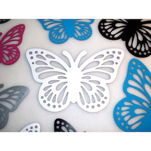 May include: A set of six decorative butterfly wall decor pieces in various colors, including white, black, pink, and blue. The butterflies are made of wood and have a delicate, intricate design.