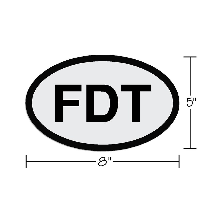 May include: A white oval sticker with a black outline and the text "FDT" in black letters. The sticker is 8 inches wide and 5 inches tall.