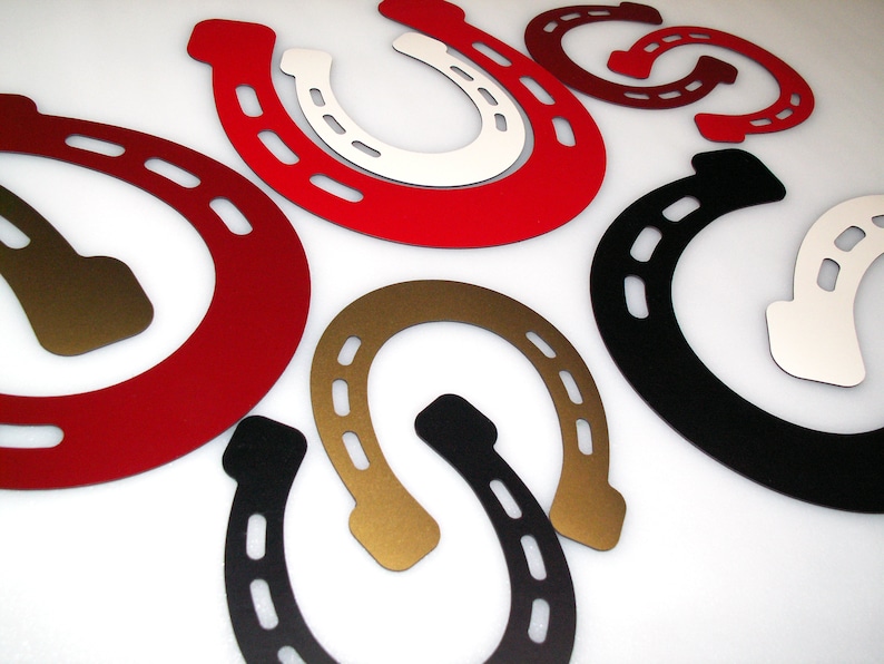 May include: A set of eight horseshoe-shaped metal wall decor pieces in various colours, including red, black, gold, and white.