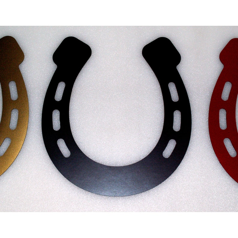 May include: Three metal horseshoes in different colours: gold, black, and red. Each horseshoe has a traditional design with nail holes.