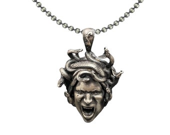 May include: A silver chain necklace with a pendant featuring a detailed sculpture of Medusa's head with snakes for hair.