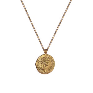 May include: A gold chain necklace with a round pendant featuring a profile of a person's face and text around the edge.