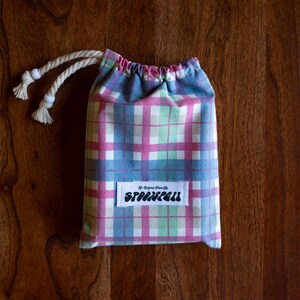 May include: A small, pink, blue, and green plaid drawstring bag with a white label that says "The Original Since 1972, Sparklefall".