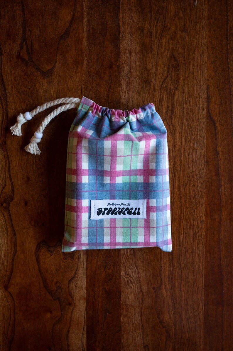 May include: A small, pink, blue, and green plaid drawstring bag with a white label that says "The Original Since 1972, Sparklefall".