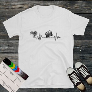 May include: White t-shirt with a black and white graphic of a heart and a film clapper board with a heartbeat line. The graphic is distressed and has a vintage look.