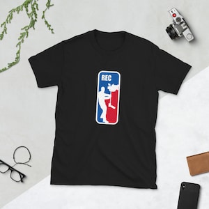 May include: Black t-shirt featuring a white graphic of a person holding a video camera. The graphic is in the style of a sports team logo with the word "REC" above the person.