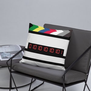 Op de afbeelding: Een wit en zwart gestreept kussen met een rood digitaal display dat de cijfers "010101010101" laat zien. Het kussen heeft een gekleurde streep aan de bovenkant met groen, geel, blauw, rood, wit en grijs.