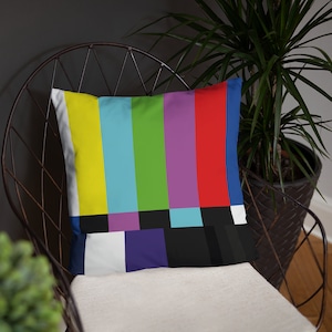 May include: A colorful throw pillow with a television test pattern design. The pillow is made of soft fabric and has a white background with colorful stripes and a black and white checkerboard pattern.