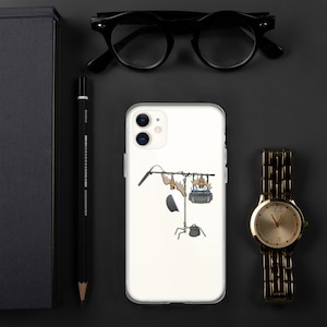 Può includere: Una custodia per iPhone bianca con un design trasparente che presenta un'illustrazione di cartoni animati di un microfono, una luce e una telecamera su un supporto. L'illustrazione è in nero, marrone e blu.