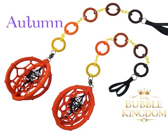 May include: Two decorative hanging ornaments with an autumn theme. Each ornament features a woven orange circle with a black web design, connected to a chain of colorful rings. The text "Autumn" is in the upper left corner.