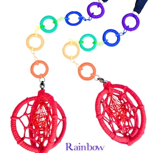 Op de afbeelding: Twee handgemaakte dromenvangers met een regenboogketting van kleurrijke ringen en een rode geweven bol. De tekst "Rainbow Into Red" staat onder de dromenvangers. Elke dromenvanger heeft een zwarte band.