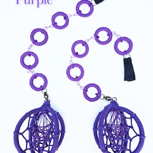 Può includere: Oggetto decorativo viola con una serie di anelli collegati e due strutture sferiche a forma di ragnatela. La parola "Purple" è visualizzata in alto a sinistra. Ha cinghie in tessuto nero e chiusure argentate.