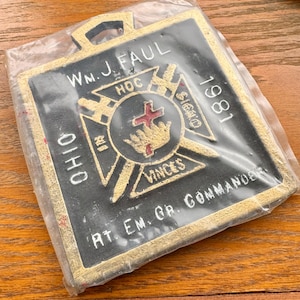 May include: A black and gold metal plaque with the text "WM. J. FAUL" and "RT. EM. GR. COMMANDER" and a Masonic symbol with a cross and the text "HOC SIGNO VINCES". The plaque also has the year "1981" and the word "OHIO".
