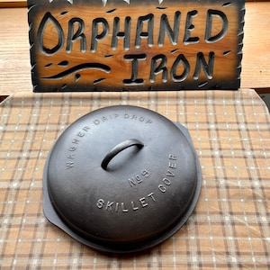 May include: A black cast iron skillet lid with the text "Wagner Drip Drop No. 9 Skillet Cover" embossed on the top.