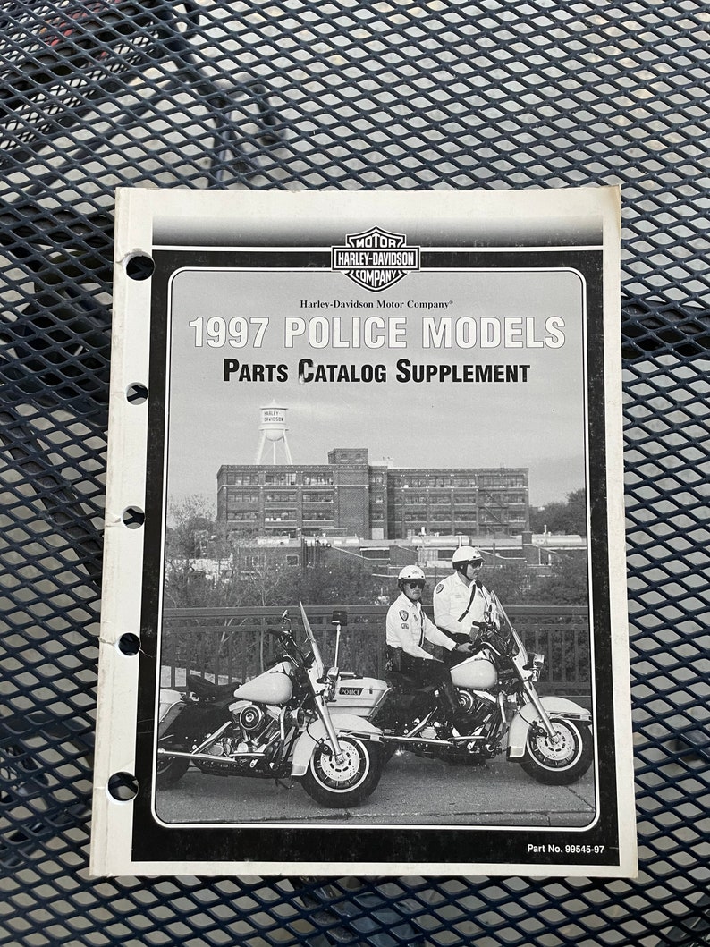 May include: A black and white photo of two Harley-Davidson motorcycles with police officers riding them. The motorcycles are parked in front of a building with a water tower on top. The text on the page reads "1997 POLICE MODELS PARTS CATALOG SUPPLEMENT" and "Part No. 99545-97".