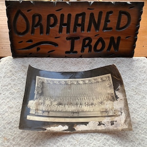 May include: Black and white photograph of a vintage iron bed frame with a woven headboard. The image is framed and has a wooden sign that reads "Orphaned Iron" above it.