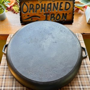 May include: A large, black cast iron skillet with the words "Jumbo Skillet" and "Made in USA" embossed on the bottom.