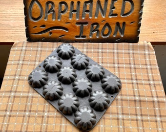 May include: A vintage cast iron muffin tin with 12 individual molds. The molds are shaped like a flower with a fluted edge. The tin is marked "Wagner" and "1238".