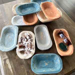 May include: A collection of nine small wooden bowls in various shades of blue, white, and brown. The bowls are rustic and have a distressed finish. Some of the bowls are filled with candy, while others are empty.