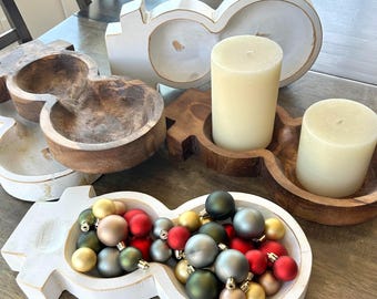 May include: White wooden snowman shaped bowl filled with red, green, and gold ornaments.  Two other wooden bowls are in the background, one with a white candle and the other with a white candle.