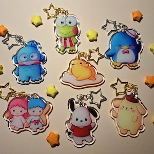 Puede incluir: Un conjunto de diez llaveros de personajes coloridos que incluyen un pez azul, una rana verde, un pollito amarillo, un pingüino azul, un perro amarillo, una niña rosa y azul, un perro blanco y tres estrellas amarillas.