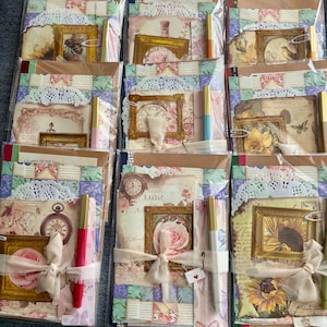 May include: A collection of vintage-themed scrapbooking kits. Each kit is packaged in a clear plastic sleeve and includes decorative papers, framed images, lace doilies, pens, and ribbons. The kits feature floral and antique clock designs.