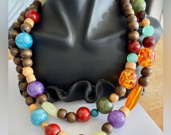 May include: A multi-strand necklace with wooden beads and colorful glass beads. The necklace features a variety of colors, including red, orange, yellow, green, blue, and purple.