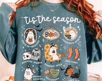 May include: Blue spruce sweatshirt with a Halloween-themed graphic. The design includes ghosts, pumpkins, bats, and the phrase "'Tis the season." Additional text includes "Trick or Treating," "Conjuring Spirits," and "Haunted Nights."