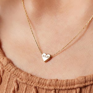 Op de afbeelding: Een goudkleurige ketting met een kleine, gepolijste hartvormige hanger. De hanger is gegraveerd met de datum 15-09-24 in een eenvoudig, donker lettertype. Het hart hangt aan een fijne, dunne goudkleurige ketting met kleine schakels.
