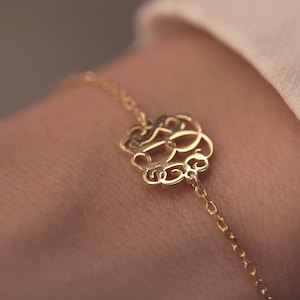 Op de afbeelding: Een delicate gouden armband met een filigraan ontwerp. Het middelpunt van de armband is een gedetailleerde, opengewerkte bedel met wervelende patronen. De ketting is fijn en de algehele esthetiek is elegant en verfijnd.