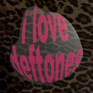 May include: Pink vinyl sticker with the text "I love Deftones" on a leopard print background.