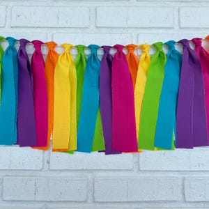 May include: A rainbow fabric banner with long, colorful fabric strips hanging down. The banner is made of different colors of fabric, including red, orange, yellow, green, blue, indigo, and violet.