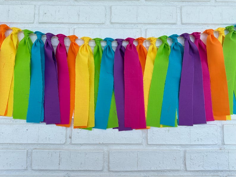 May include: A rainbow fabric banner with long, colorful fabric strips hanging down. The banner is made of different colors of fabric, including red, orange, yellow, green, blue, indigo, and violet.