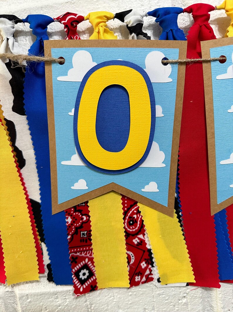 K&ouml;nnte beinhalten: Ein Banner mit einem Hintergrund aus blauem Himmel und wei&szlig;en Wolken. Die Zahl "0" ist gelb mit einem blauen Umriss. Das Banner ist mit roten, gelben und blauen Stoffstreifen verziert.
