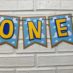 K&ouml;nnte beinhalten: Ein Banner mit dem Wort "ONE" in gelben Buchstaben mit blauen Umrandungen auf blau-wei&szlig;em Hintergrund. Das Banner ist aus Papier und hat einen braunen Rand.