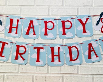May include: A blue and red banner with the words "Happy Birthday" in red letters. The banner has a cloud pattern and red airplanes on each end.