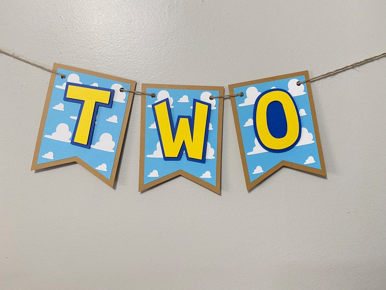 K&ouml;nnte beinhalten: Ein braunes und gelbes Banner mit dem Wort "ZWEI" in gelben Buchstaben mit blauen Umrandungen. Das Banner hat einen blauen und wei&szlig;en Hintergrund mit einem Wolkenmuster.