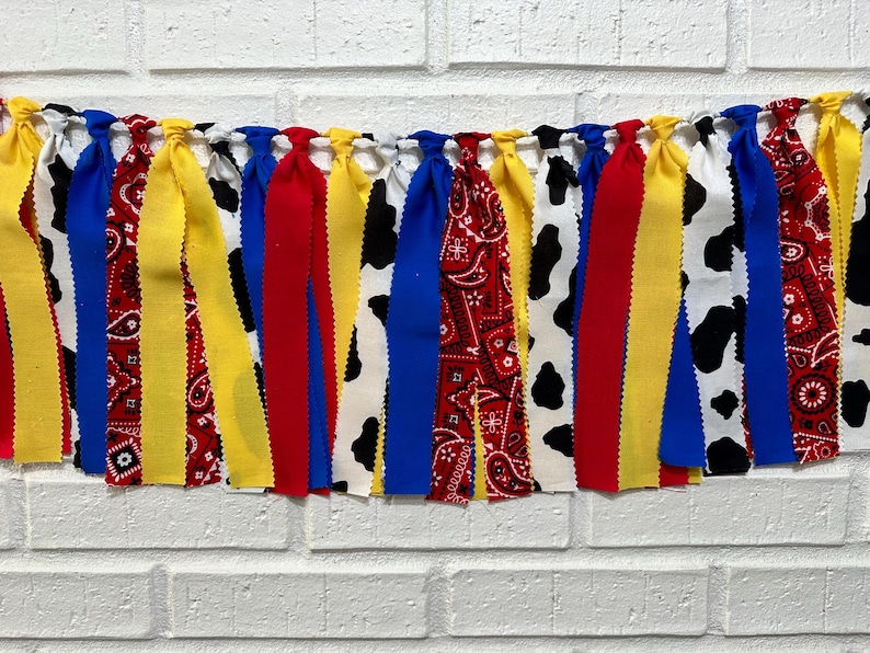K&ouml;nnte beinhalten: Ein farbenfrohes Stoffbanner mit roten, gelben, blauen und wei&szlig;en Streifen. Das Banner zeigt ein Kuhmuster und ein rotes Bandanamuster.