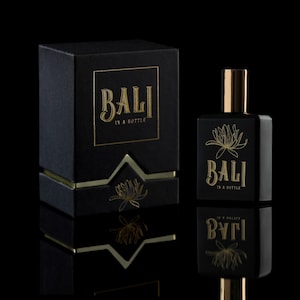May include: A black box with gold lettering that reads "BALI IN A BOTTLE" and a black bottle with gold lettering that reads "BALI IN A BOTTLE" and a gold floral design.