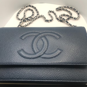 May include: A navy blue leather wallet-on-chain bag with a silver chain strap. The bag features a textured surface and a raised interlocking double-C logo on the front.