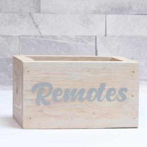 May include: A light wood box with the word "Remotes" printed in grey on the front.