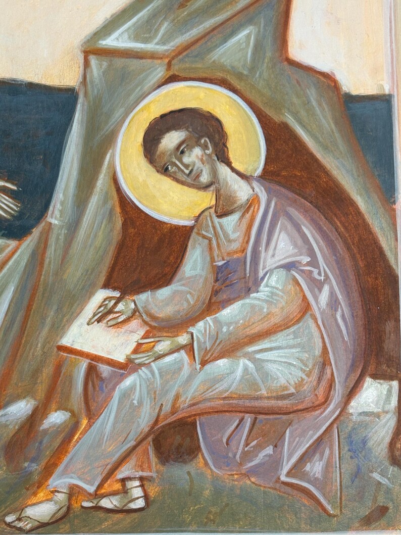 May include: An icon painting depicting a figure with a golden halo, dressed in white and lavender robes, seated and writing on a parchment. The artwork features warm tones of brown, orange, and beige, with a focus on the figure's contemplative expression.