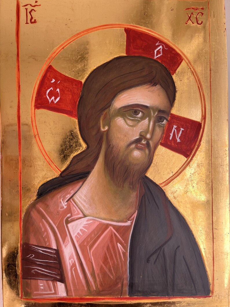 May include: An icon depicting a figure with brown hair and a beard, wearing a pink robe and a dark cloak. A red halo with a cross shape surrounds the figure's head. The background is gold.