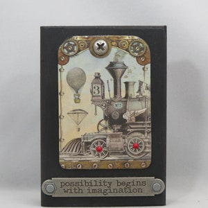 May include: A black wooden plaque with a vintage illustration of a steampunk train with hot air balloons and the text "possibility begins with imagination". The plaque is decorated with metal accents and a gold screw.