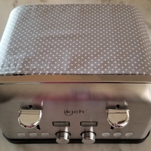 May include: A silver two-slice toaster with a gray and white polka dot fabric cover. The toaster has a brand name "ikich" on the front.