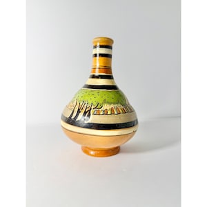 May include: A hand-painted ceramic vase with a bulbous body and a narrow neck. The vase features a landscape design with trees and a green field, accented by black and tan stripes. The base is a light brown color.