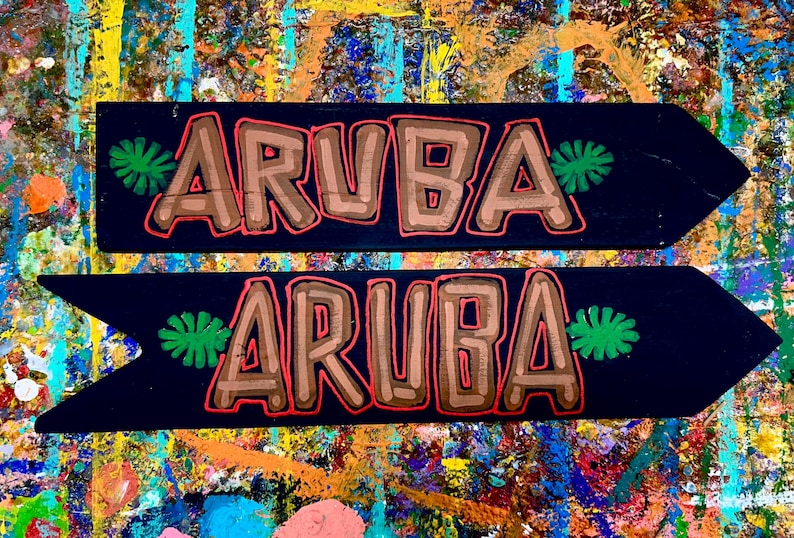 K&ouml;nnte beinhalten: Zwei schwarze Holzpfeil-Schilder mit dem Wort "ARUBA" in braunen Buchstaben, die rot umrandet sind. Auf jedem Schild befinden sich gr&uuml;ne Blattmotive. Die Schilder befinden sich auf einem farbenfrohen, abstrakten Hintergrund.